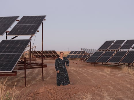 A woman stands in the middle of a field of solar panels