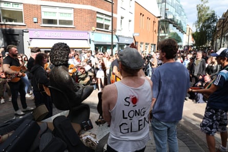 People, one with a shirt that says ‘So long Glen’ stop too listen as musicians play