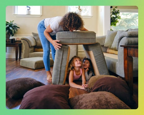 A woman builds a pillow fort with two children on a living room floor