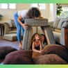 A woman builds a pillow fort with two children on a living room floor