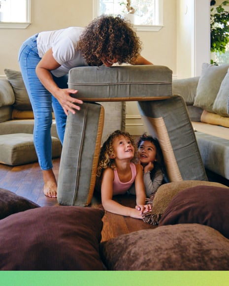 A woman builds a pillow fort with two children on a living room floor