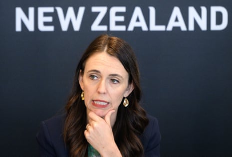 Jacinda Ardern looking thoughtful in front of a backdrop with the words New Zealand on it