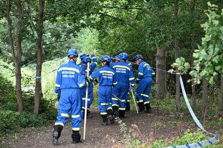 Members of HM Coastguard Search and Rescue in bright blue overalls walk down a path between trees.