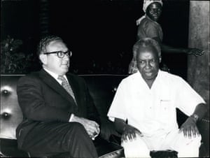 Kissinger sitting next to an angry-looking African man in a white shirt