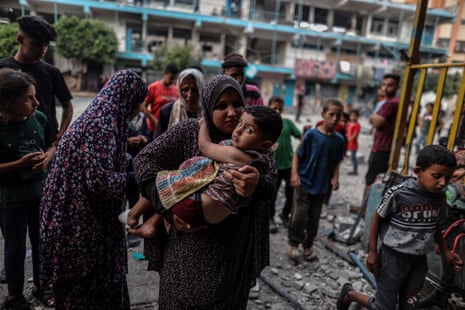 A Palestinian woman holding a boy is seen among scattered rubble and wreckage.