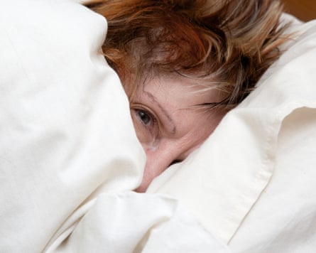 Mature woman snuggled up in bed one eye open peering from under the duvet