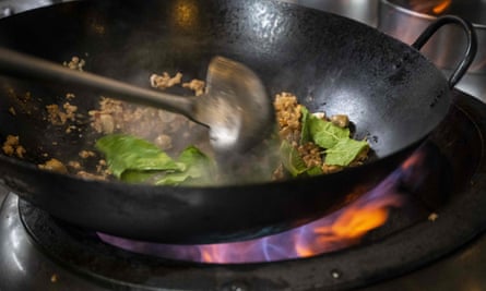 Meat and leafy greens being stir fried in a wok.