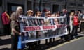 A line of people outside Central Hall, Westminster, hold up a banner. It features photos, names and ages of victims of the infected blood scandal with the words “MURDERED MURDERED MURDERED”