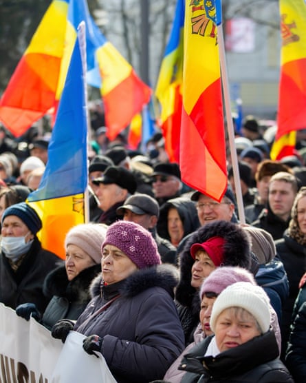 Un grup de femei în mare parte de vârstă mijlocie ținând un banner sub o mare de steaguri moldovenești.
