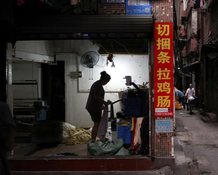 A person is shown in silhouette working with fabric at a machine against a white wall, with Chinese characters on a pillar in the foreground
