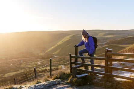 A young woman walks over a stile at sunrise