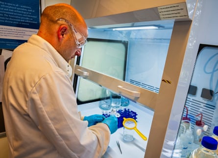 Man in white lab coat with goggles works with samples