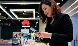 A woman looking at a Huawei smartphone Huawei sign in background at CES in Las Vegas.