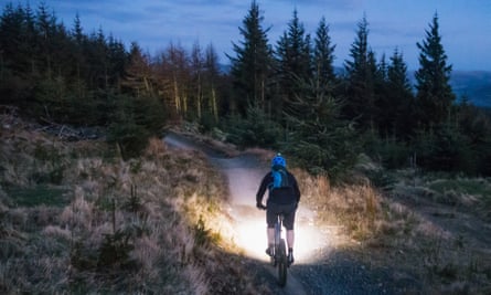 Mountain biking with lights at dusk. Rear view of a man using bright lights to illuminate the mountain bike trail in front of him as daylight fades.