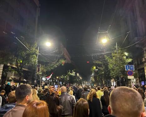 Crowds fill a dark Belgrade street at night celebrating the election result, flags raised overhead