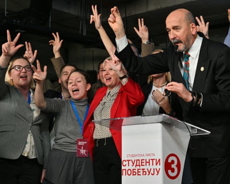 Radomir Saicic speaks at a podium as cheering supporters raise victory signs celebrating election win
