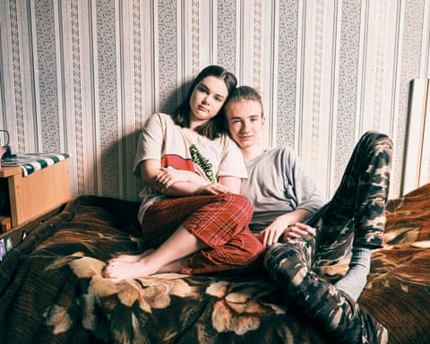 Male and female teenagers relax on a bed together, looking to camera