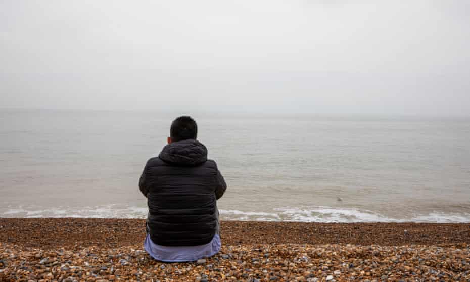 Mohammad sitting on pebbly beach looking out to sea