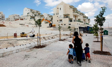 A woman walks with children past apartments under construction in the West Bank Jewish settlement of Maale Adumim.