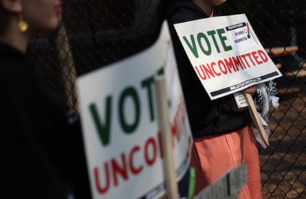 people hold signs saying ‘vote uncommitted’ in green and red