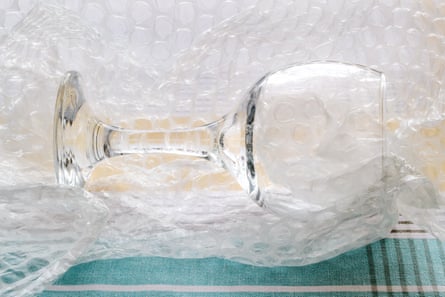 A transparent glass goblet lies in bubble wrap on a white and blue checkered tablecloth.