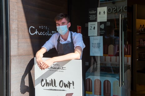 A Hotel Chocolat worker stands at the entrance of one of its stores, wearing a face mask.