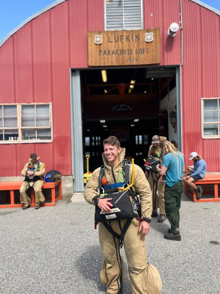 A man smiles in a smokejumping uniform in front of a large building.