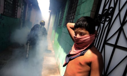 A child protects himself as sanitation workers fumigate San Salvador’s El Campito slum to kill mosquitoes.
