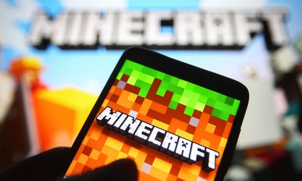 A Minecraft logo is seen on a smartphone screen and also in the background