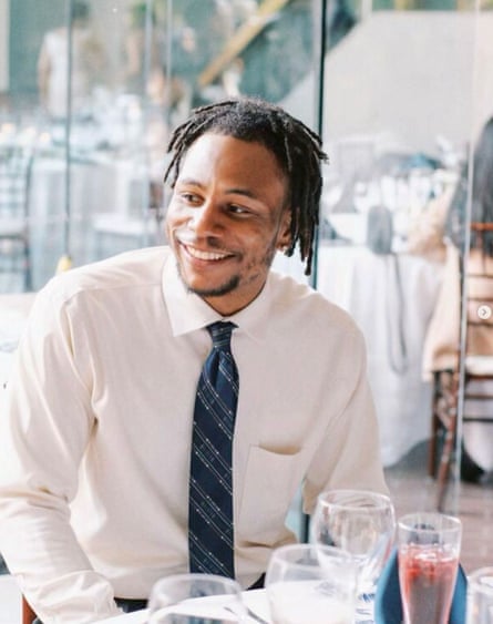A man with a wide smile who is wearing a tie and white dress shirt sits in a sunlit restaurant.
