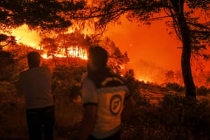 Two emergency responders are in the foreground as flames burn on a hillside and among trees in the near distance