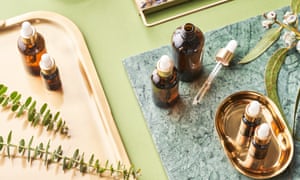 From above bottles of essential oils and twigs of plants placed on metal tray and marble board during aromatherapy and spa session on green background
