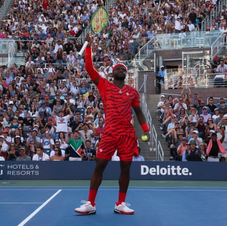 Tiafoe in all-red with tiger-like stripes. He holds his racket up to the crowd for their response.