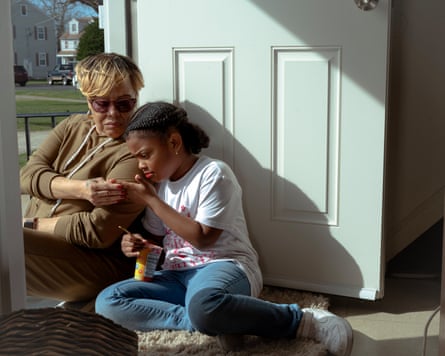 Middle-aged Black woman with frosted blond bob, sitting in sunny front doorway with a Black girl, maybe 10 years old, in a white T-shirt and jeans, seen from inside the house.