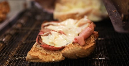 closeup of an open face ham and cheese sandwich on a conveyor belt