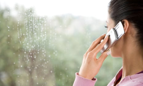 Close-up of a young woman looking out of a rainy window, talking on a mobile phone.