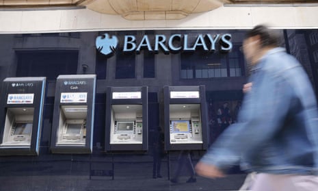 A pedestrian walks past a row of ATMs outside a branch of British bank Barclays in central London