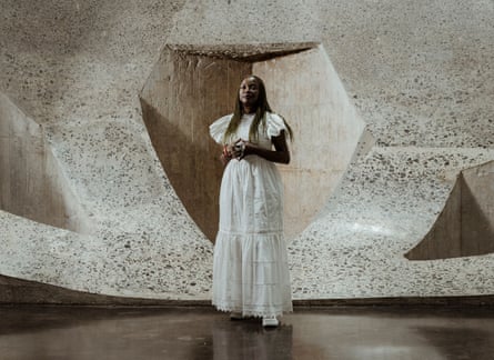 Koyo Kouoh wearing a white dress standing in front of stone sculpture in a museum