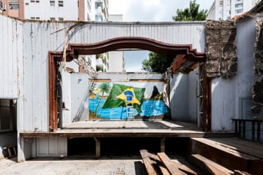 A roofless outdoor room made of wood with a Brazil flag on the back wall with a ladder leaning against it