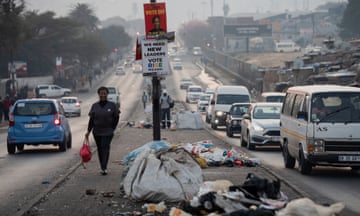 A woman walks past piles of uncollected trash in the township of Alexandra