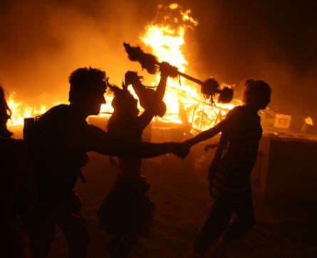 People dance in front of a large bonfire