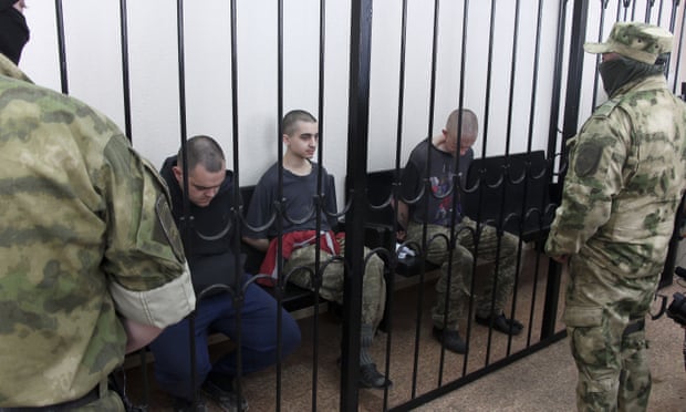 Aiden Aslin, left, Shaun Pinner, right, and Moroccan Brahim Saaudun, centre, behind bars in a courtroom in Donetsk.