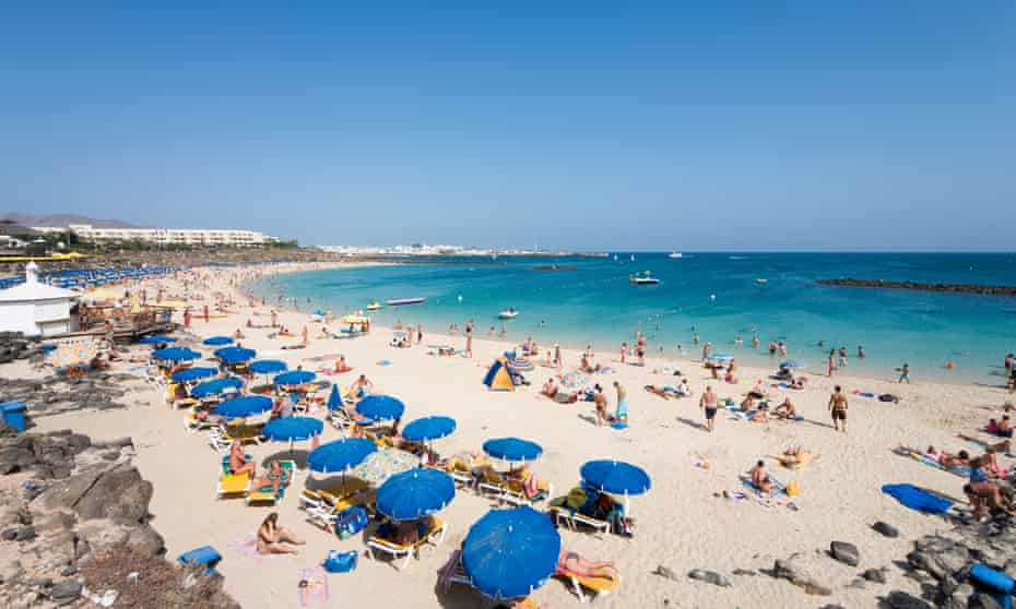 The main beach, Playa Blanca, in Lanzarote, filled with holidaymakers on the sand and under beach umbrellas. Canary Islands, Spain.