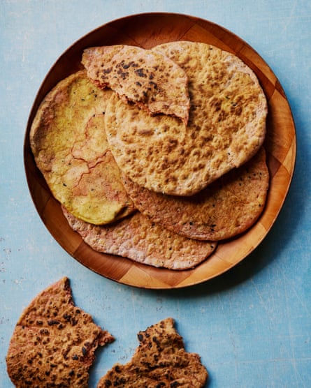 Flatbreads on a wooden plate, with a torn-up flatbread beside the plate, on a blue table
