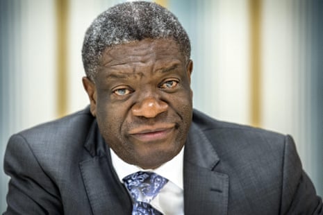 Greying African man wearing a suit jacket, shirt and tie looks at camera