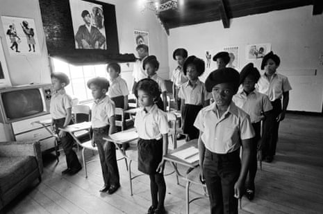 Schoolchildren in uniform stand at schooldesks.