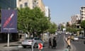 People cross a road lined with apartment blocks and with a sign about Iran's missile capability