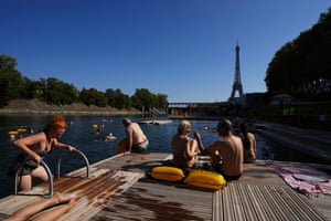 A woman climbs out of the River Seine on a sunny day, with the Eiffel Tower rising in the background