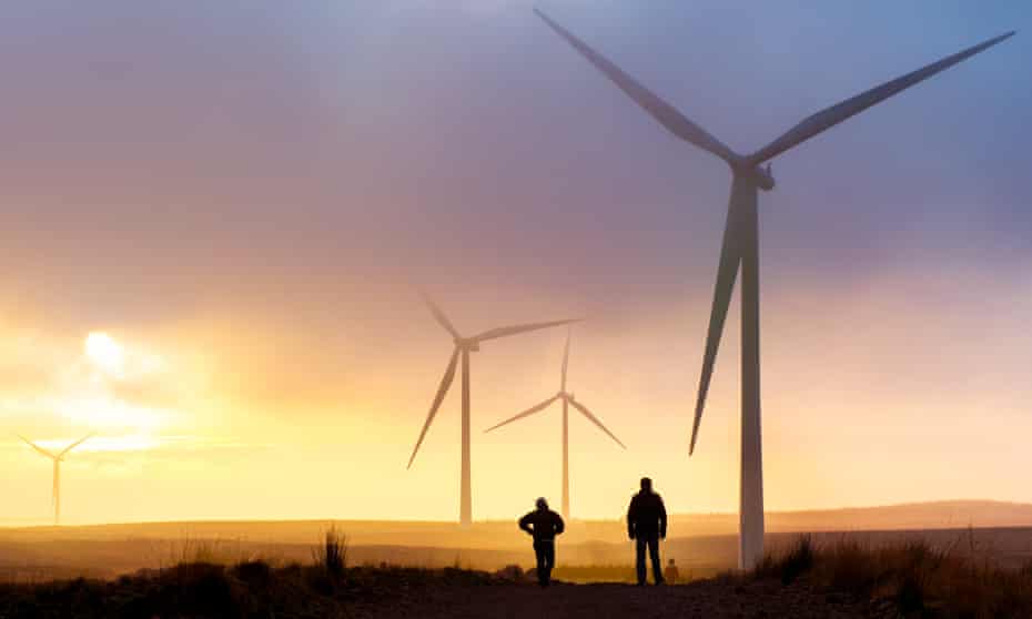 Couple silhouette at sunset standing on a ridge of a trail in a windfarm