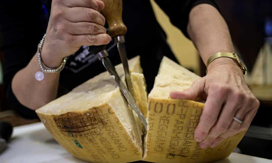 A woman cuts open a wheel of Parmigiano Reggiano cheese